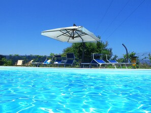 Una piscina con agua azul cristalina, rodeada de sillas de descanso y un gran paraguas.