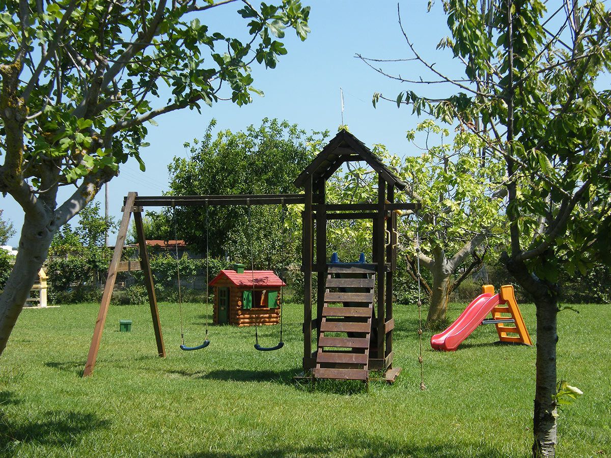 A playground with a wooden swing set, a slide, and a small playhouse.
