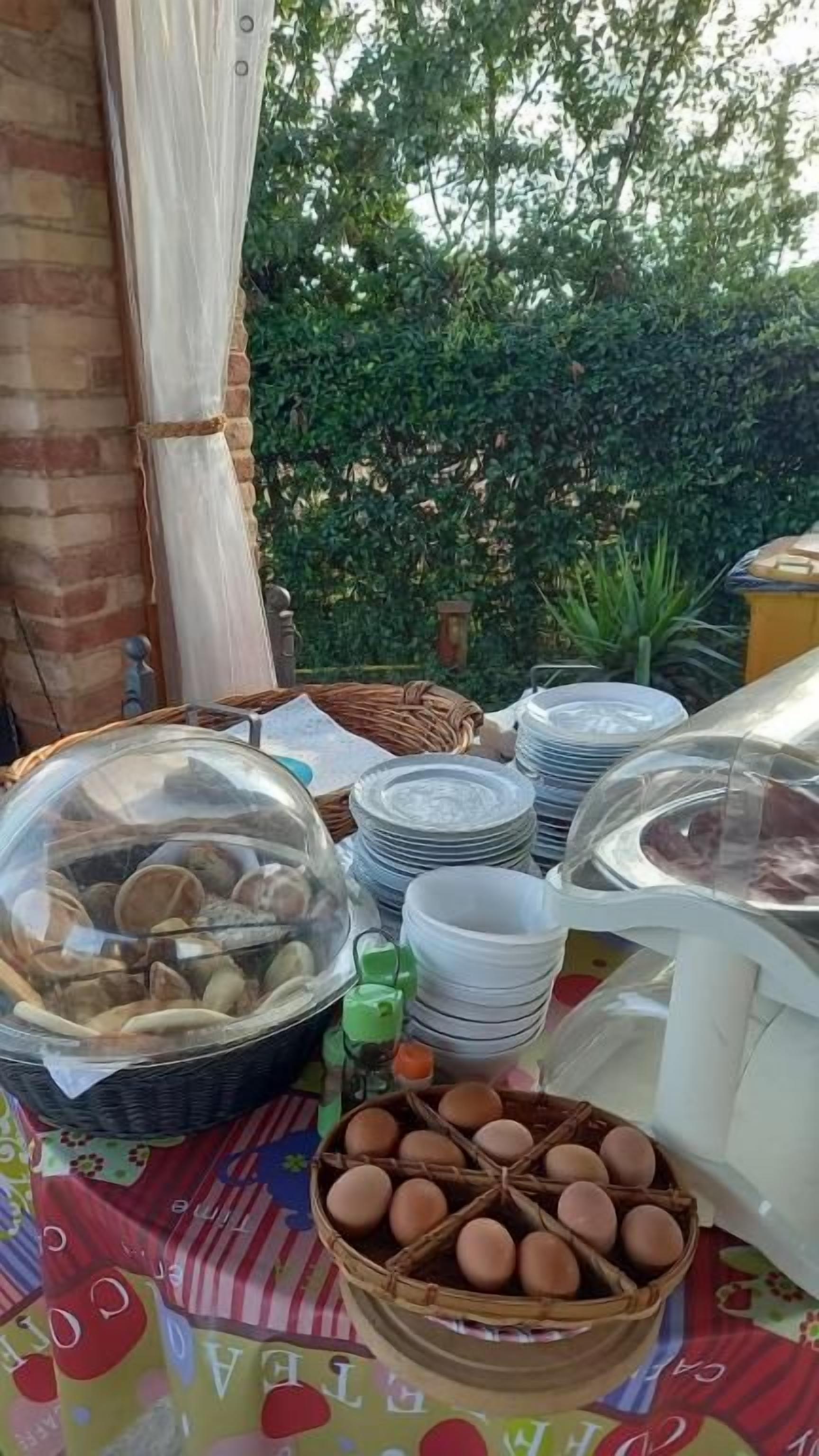 A table with food items and plates, possibly for a buffet or catering service, set outdoors with a brick wall and greenery in the background.
