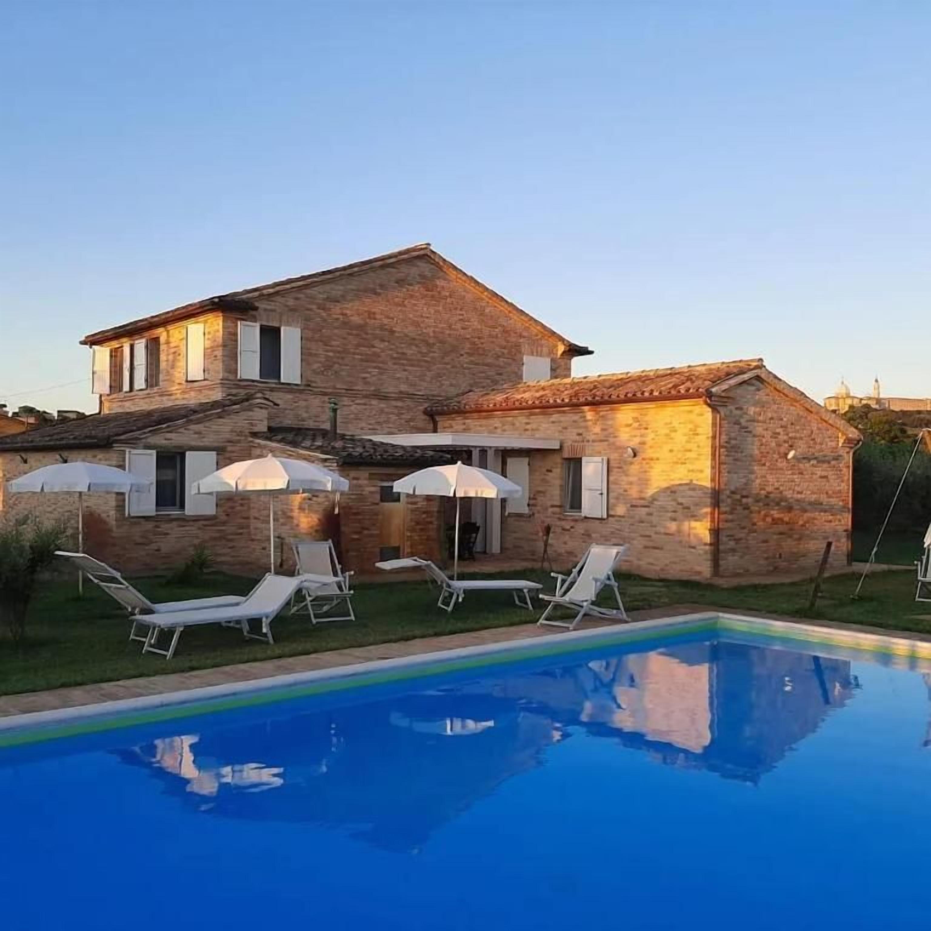 Una casa de piedra de dos pisos con piscina, mobiliario exterior y cielo despejado.