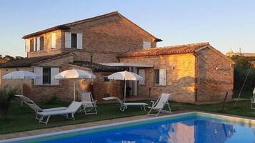 Una casa de piedra de dos pisos con piscina, mobiliario exterior y cielo despejado.