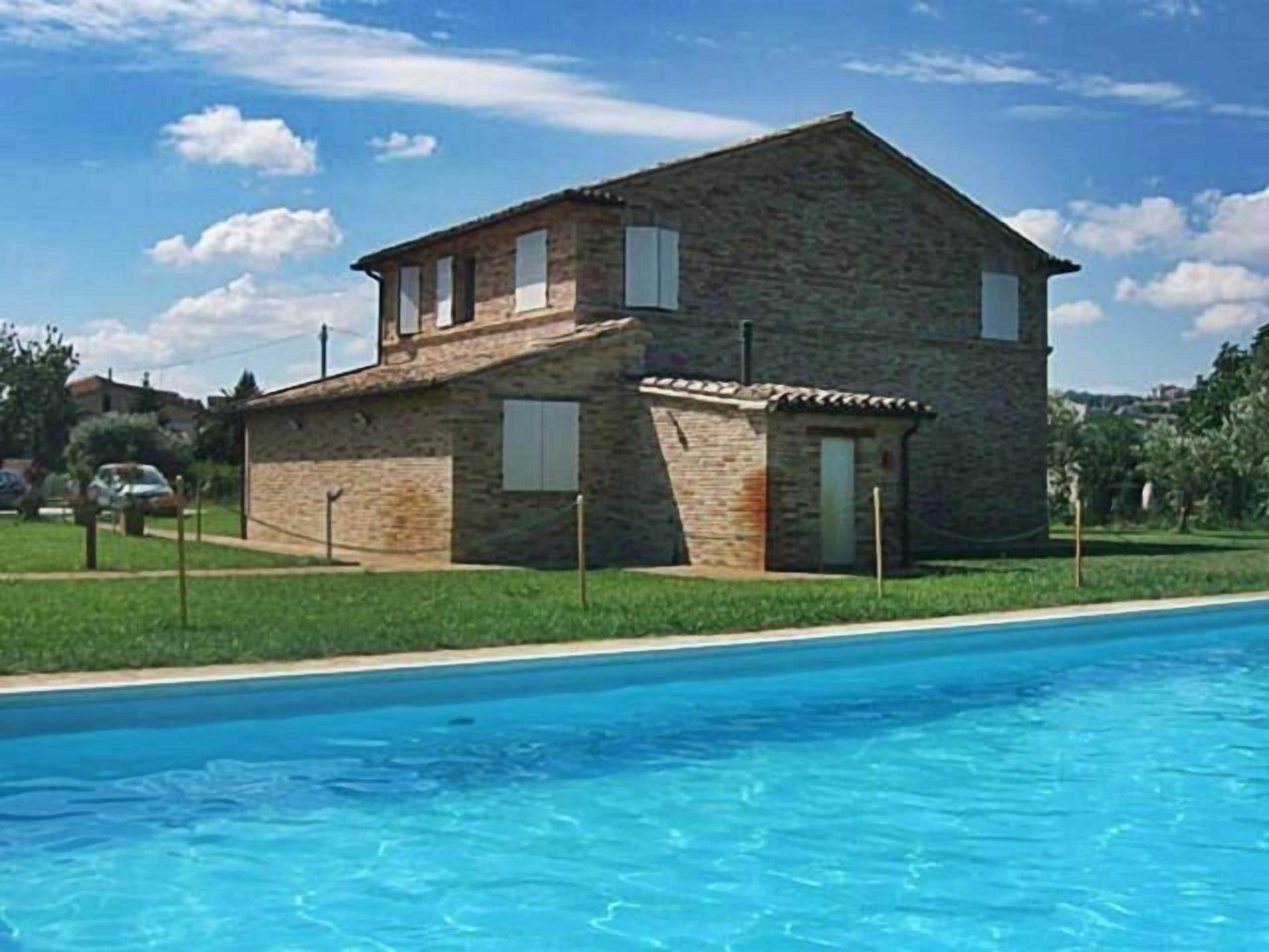 Ein zweistöckiges Steinhaus mit Schwimmbecken davor.