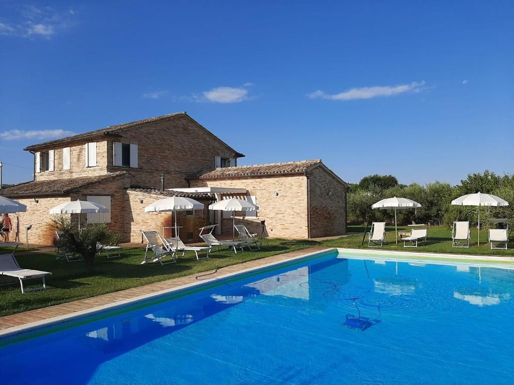 A swimming pool with lounge chairs and umbrellas, a brick building with a tiled roof, and a clear blue sky.