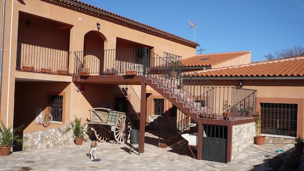 Un edificio de dos pisos con un patio de piedra, un carro de madera y un perro.