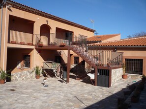 Un bâtiment à deux étages avec une cour intérieure en pierre, une charrette en bois et un chien.