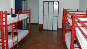 Una habitación tipo dormitorio con literas, un armario y un cubo de basura.