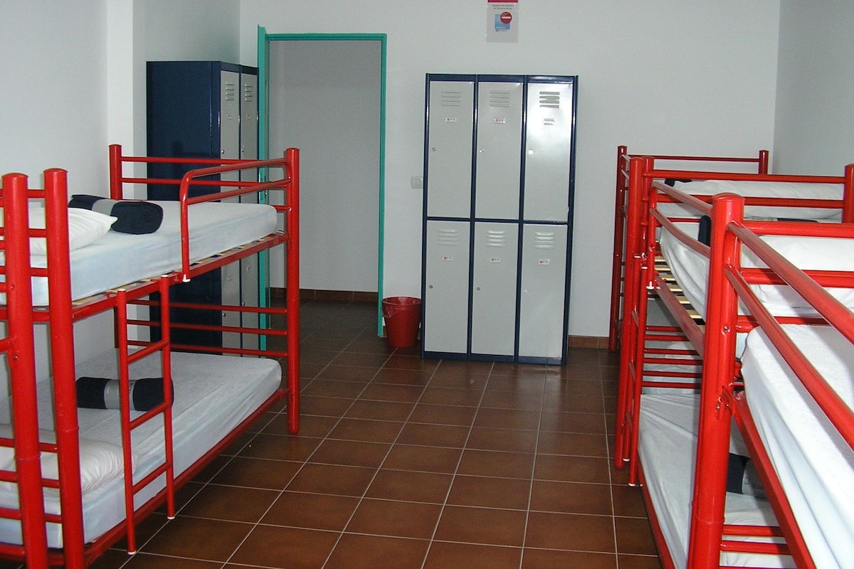 Una habitación tipo dormitorio con literas, un armario y un cubo de basura.