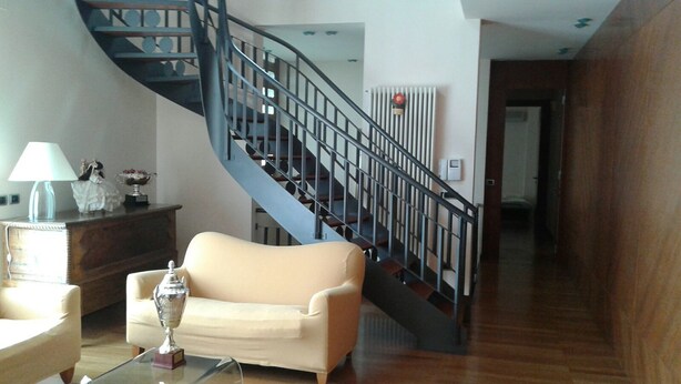 A living room with a beige sofa, a glass coffee table, a lamp, and a staircase with a black railing. - B&B Paradiso (Loreto)