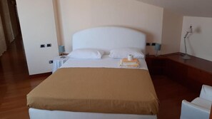 Hotellihuone, jossa on suuri sänky, yöpöytä lampun kanssa ja tuoli.