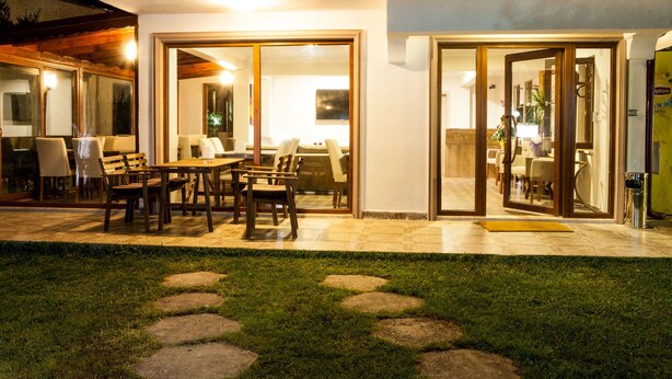 Un patio con mesa y sillas, un pequeño jardín con losetas y un ventanal que da a un espacio interior.