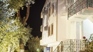 Una entrada de hotel bien iluminada con una escalera, un letrero y un camino bordeado de árboles.