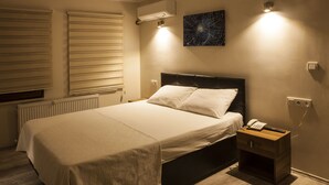 Una cama bien tendida con sábanas blancas en una habitación con suelo de madera, un radiador y aire acondicionado de pared.