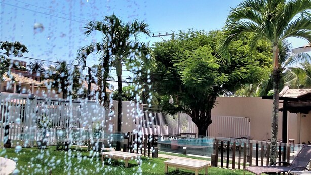 A pool area with a clear sky, palm trees, and a fenced garden. - Pousada Praia do Flamengo (Salvador)