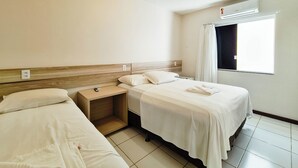 A hotel room with two beds, a nightstand, a window with curtains, and a ceiling light. - Pousada Praia do Flamengo (Salvador)