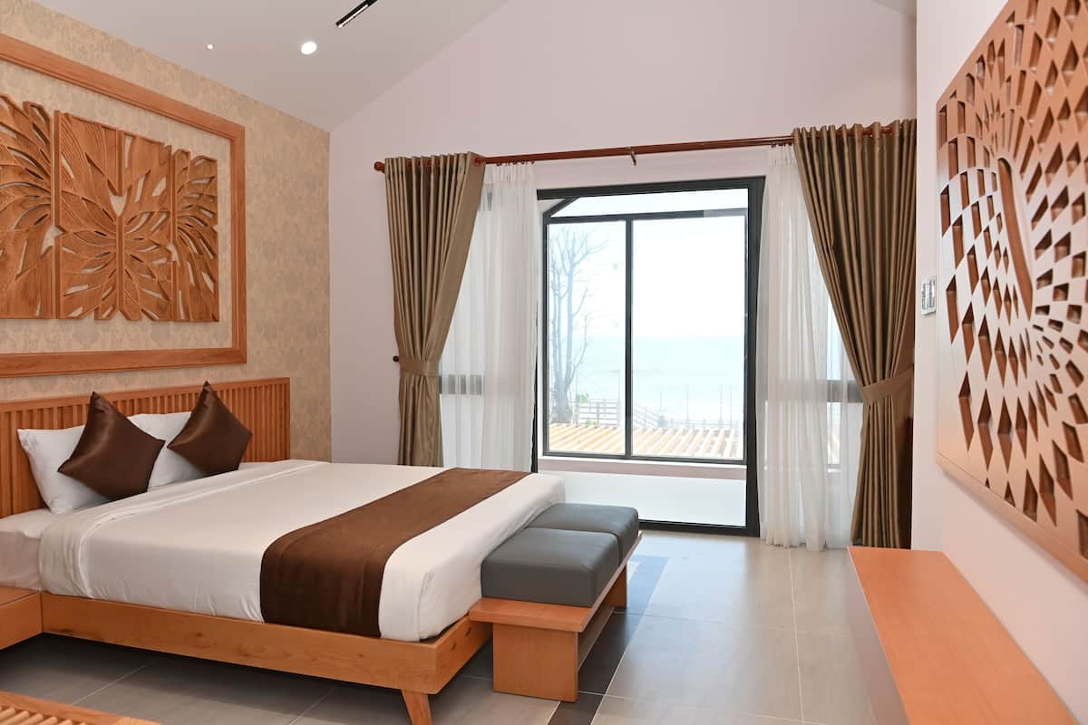 Ein modernes Hotelzimmer mit einem großen Bett, einem Holzkopfende, einer Bank und Meerblick durch ein großes Fenster.