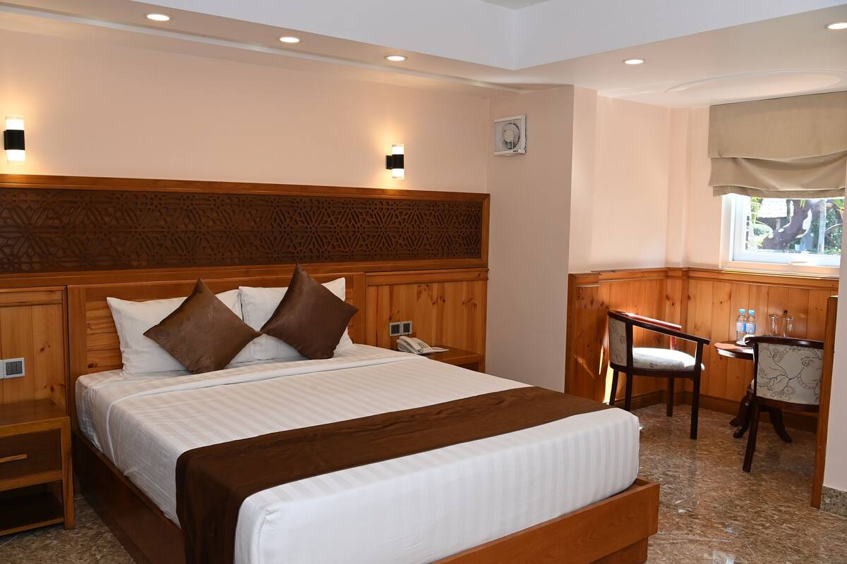 Ein Hotelzimmer mit einem großen Bett, einem Holzkopfstück, Nachttischen, einem Schreibtisch mit Stühlen und einem Fenster mit Aussicht.