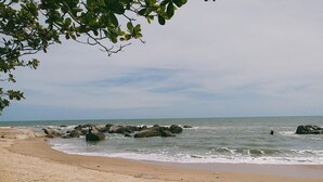 Une plage de sable avec de gros rochers dans l’eau et un ciel dégagé.