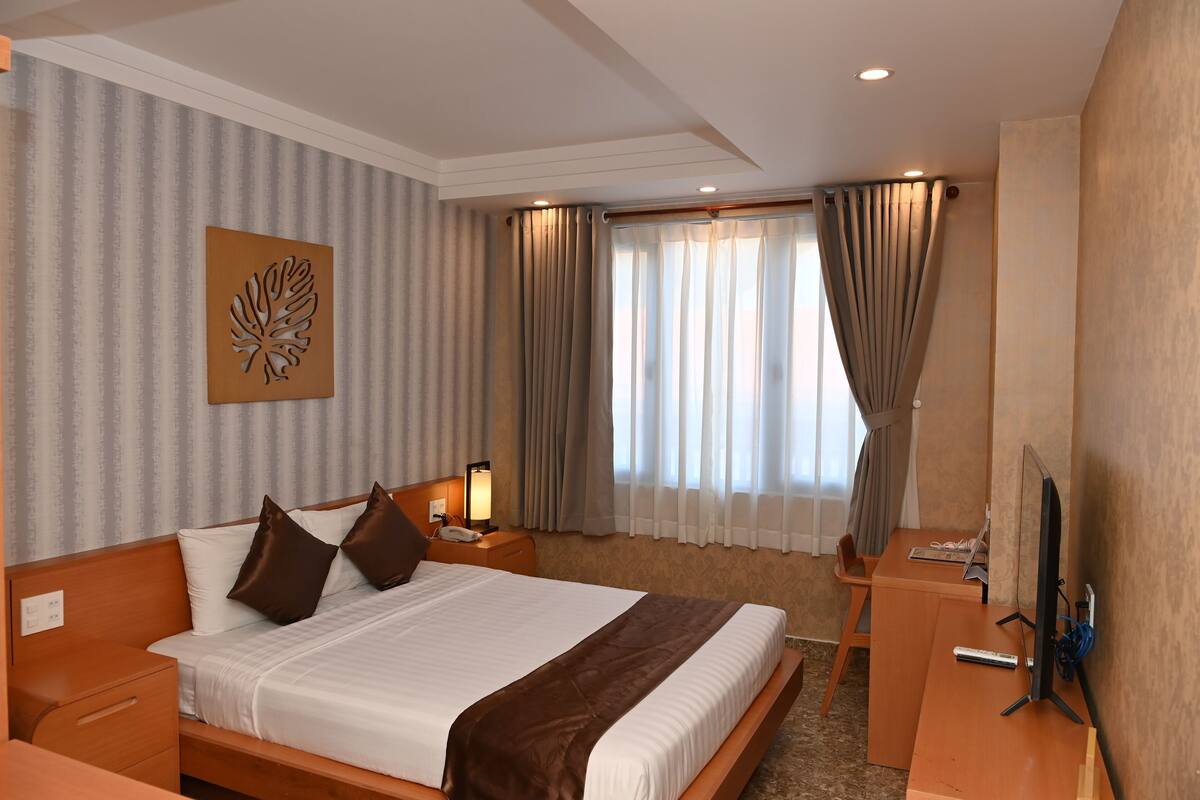 Ein Hotelzimmer mit einem großen Bett, einem Schreibtisch, einem Stuhl, einem Fernseher und einem Fenster mit Vorhängen.