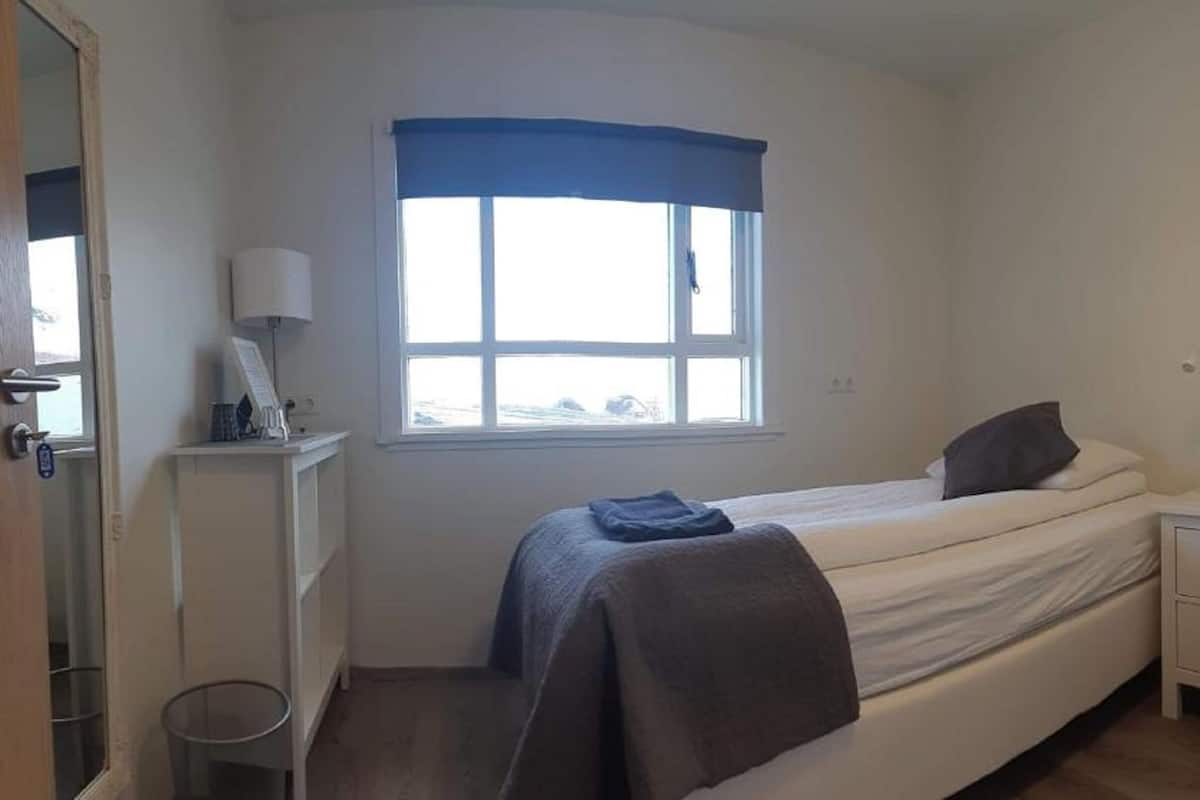 Une chambre à coucher comprenant un lit, une table de chevet, une chaise, une fenêtre et un tableau encadré au mur.