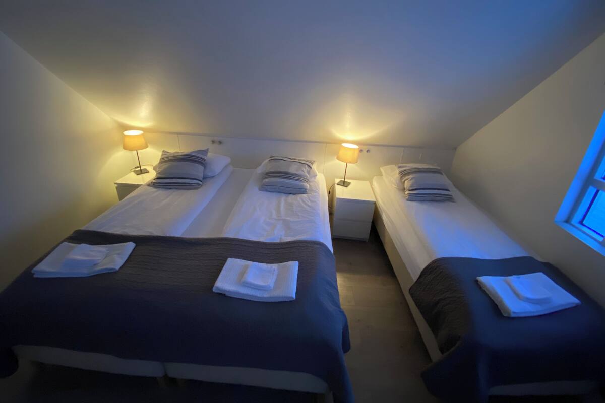 Une chambre avec trois lits simples, chacun étant équipé d’une table de chevet et d’une lampe.
