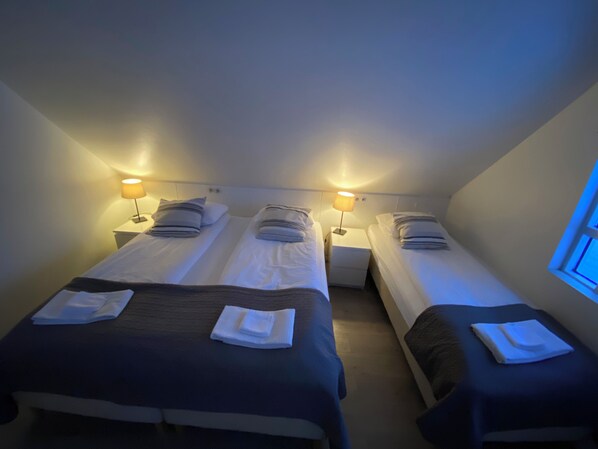 Una habitación con tres camas individuales, cada una con una mesita de noche y una lámpara.