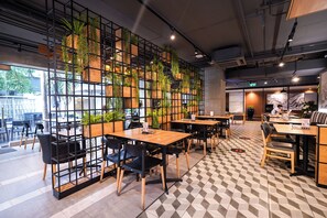 L’intérieur d’un café moderne, avec des tables en bois, des chaises noires et un mur vert orné de plantes.