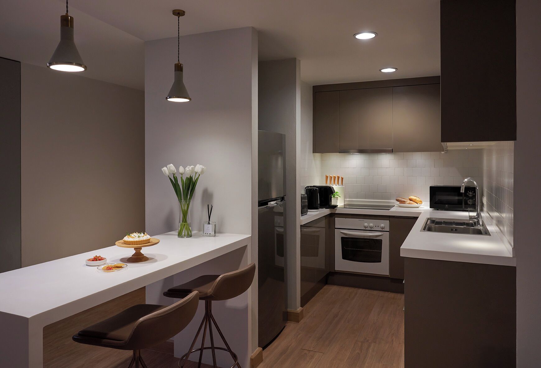 A modern kitchen with a white countertop, two pendant lights, a built-in oven, and a microwave.