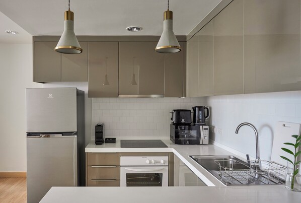 Une cuisine moderne dotée d’appareils électroménagers en acier inoxydable, d’un four encastré, d’une machine à café et de luminaires suspendus.