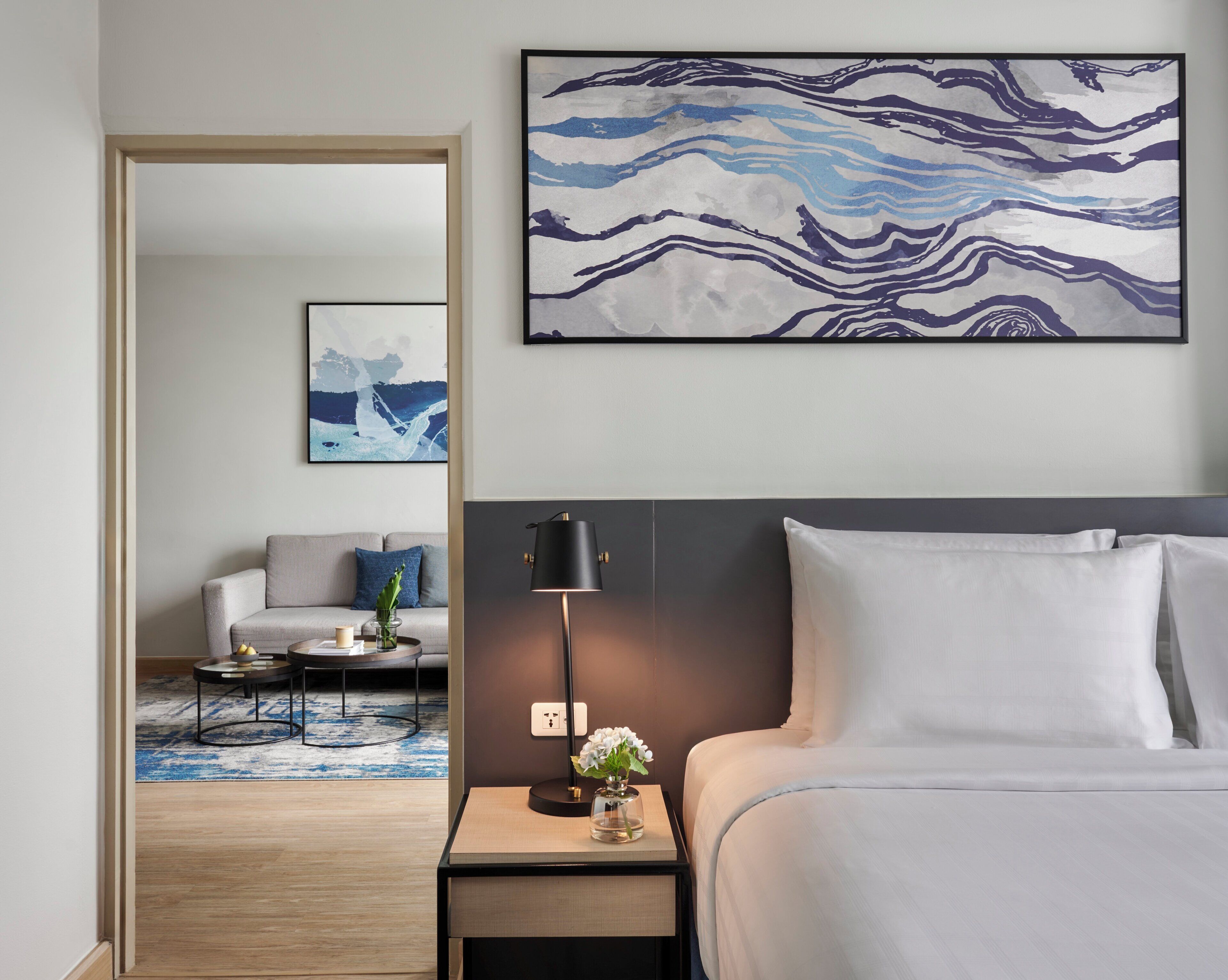 Een hotelkamer met een bed, nachtkastje, lamp en kunst aan de muur.