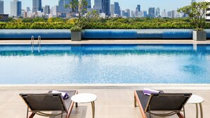 A rooftop pool with two lounge chairs and a city skyline view.