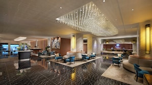 Un hall d’entrée spacieux avec un comptoir d’accueil, des espaces de détente et un lustre moderne.