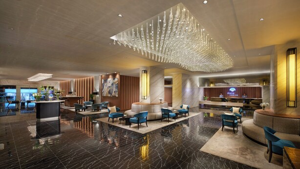 A spacious lobby with a reception desk, seating areas, and a modern chandelier.
