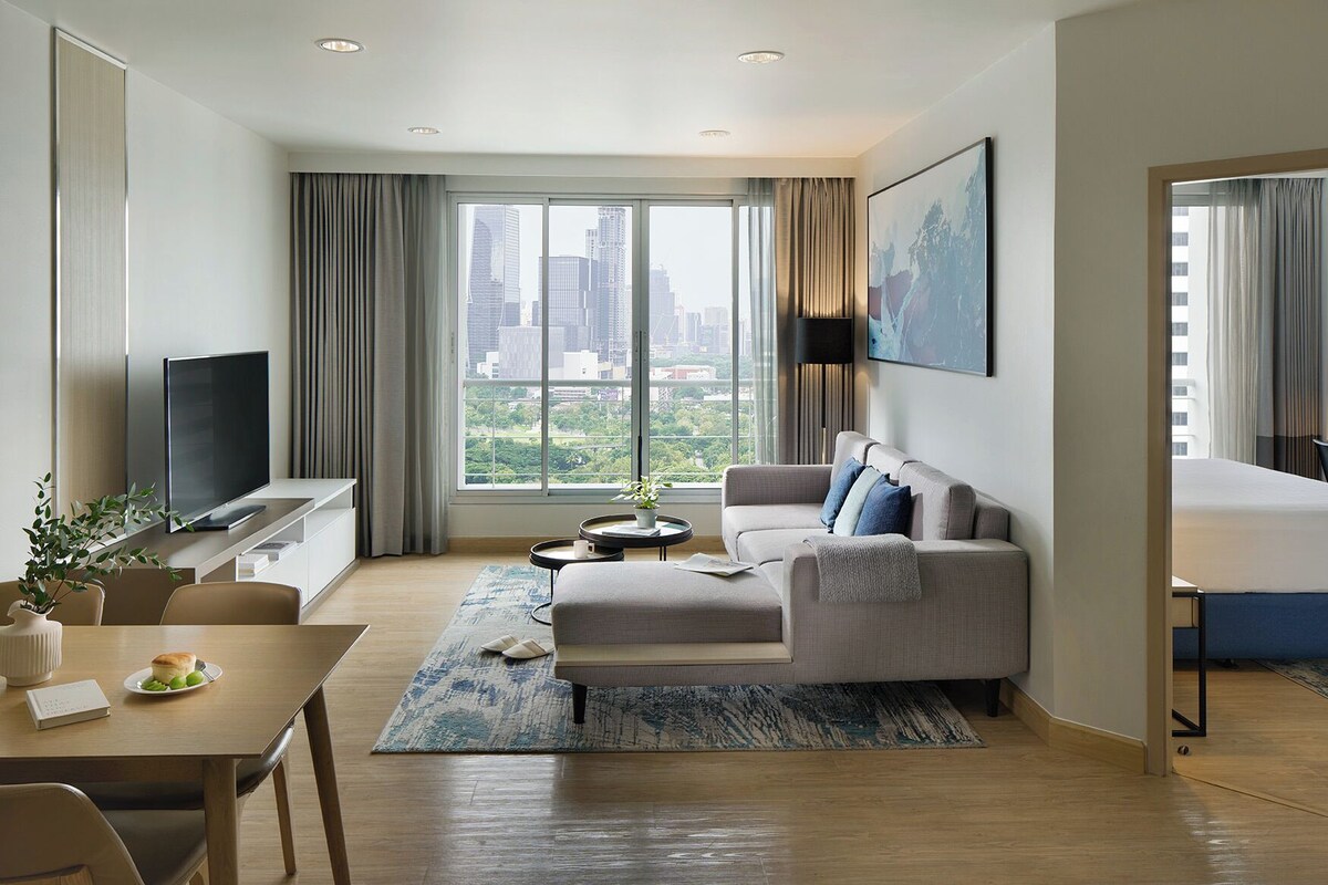 Una habitación de hotel moderna con vistas a la ciudad, televisión de pantalla plana, sofá, zona de comedor y cama.