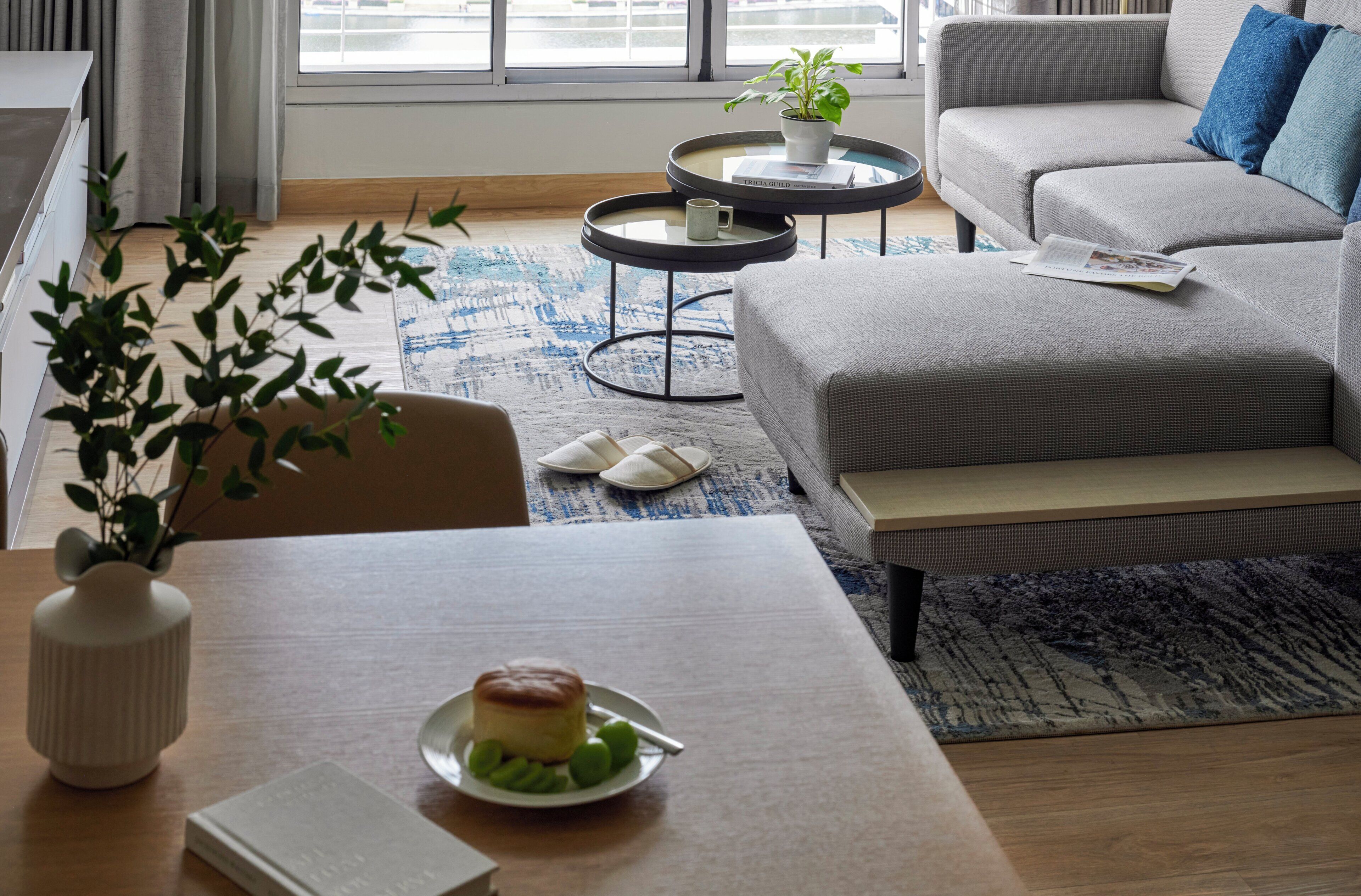 A modern living room with a sofa, coffee table, and a dining table with a plant and a plate of food.