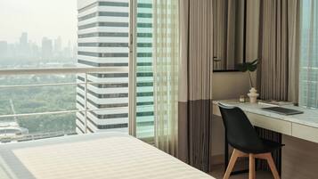 A modern hotel room with a large window, a desk with a laptop, a black chair, and a bed.