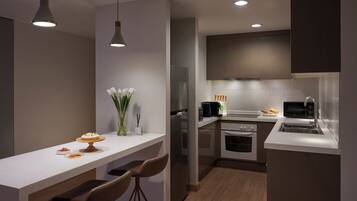 A modern kitchen with a white countertop, two pendant lights, a refrigerator, a microwave, and a sink.