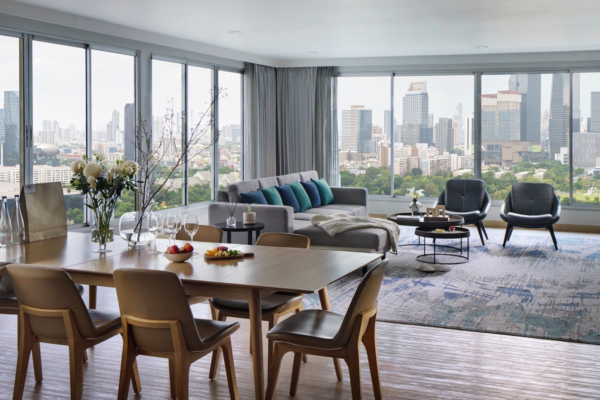 Un salon moderne avec un coin repas, de grandes fenêtres offrant une vue sur la ville et un panorama urbain visible à travers ces fenêtres.