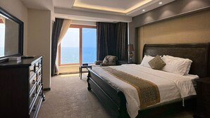 A hotel room with a large bed, a dresser, a bench, and a view of the ocean. - Al-Borg Al-Watheer Serviced Apartments (Jizan)