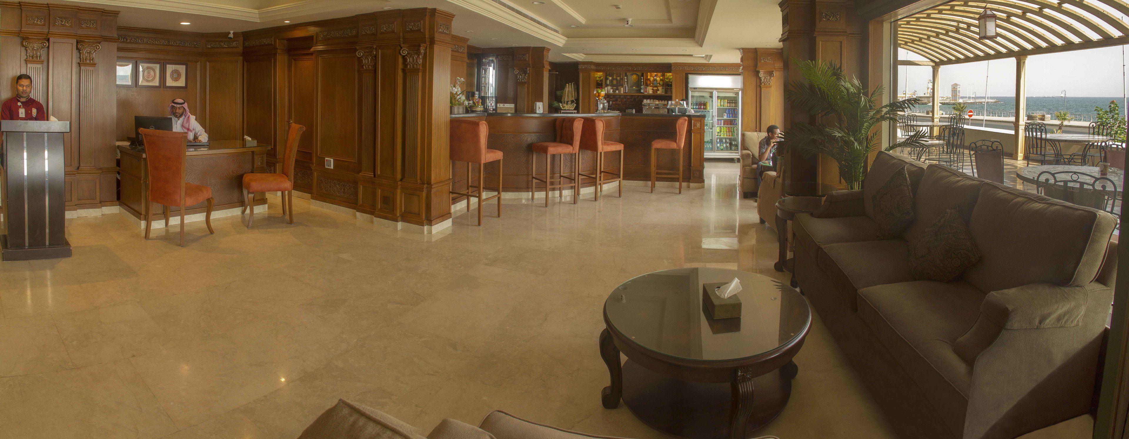 Un hall con mostrador de recepción, zona de bar, asientos y vista al mar.