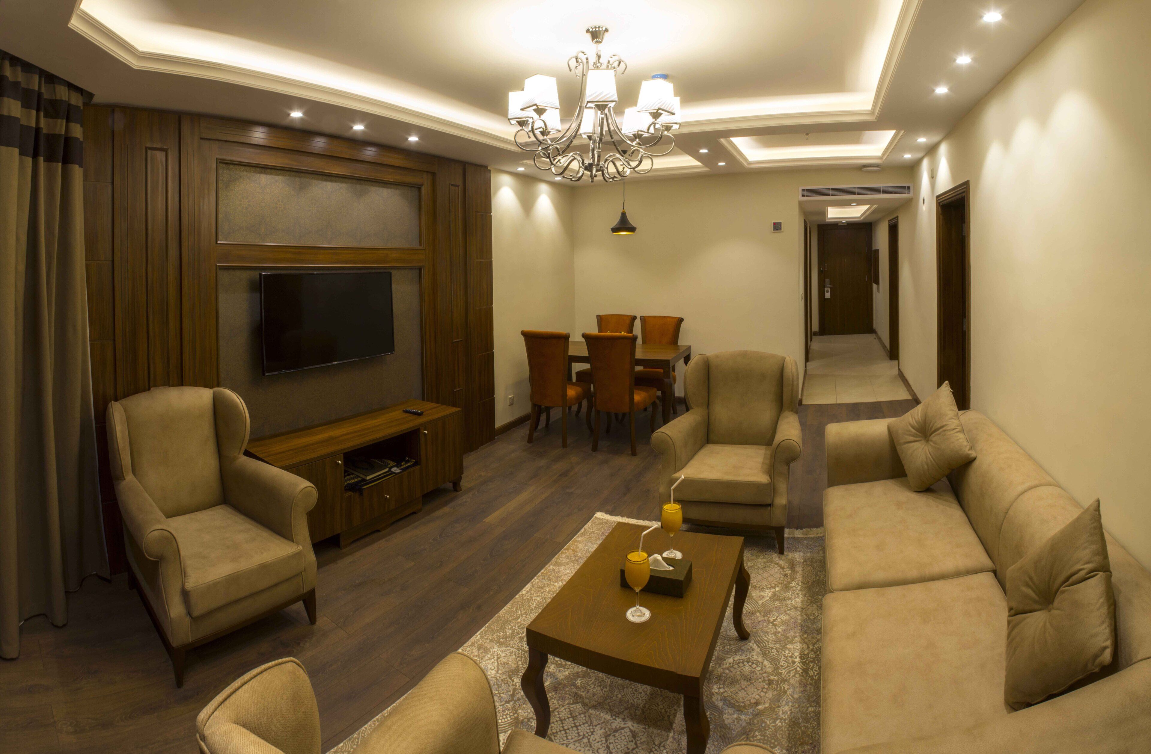 Una sala de estar con televisión de pantalla plana, sofá, sillones, una mesa de centro y una araña.
