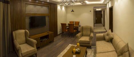 Una sala de estar con televisión de pantalla plana, sofá, sillones, una mesa de centro y una araña.