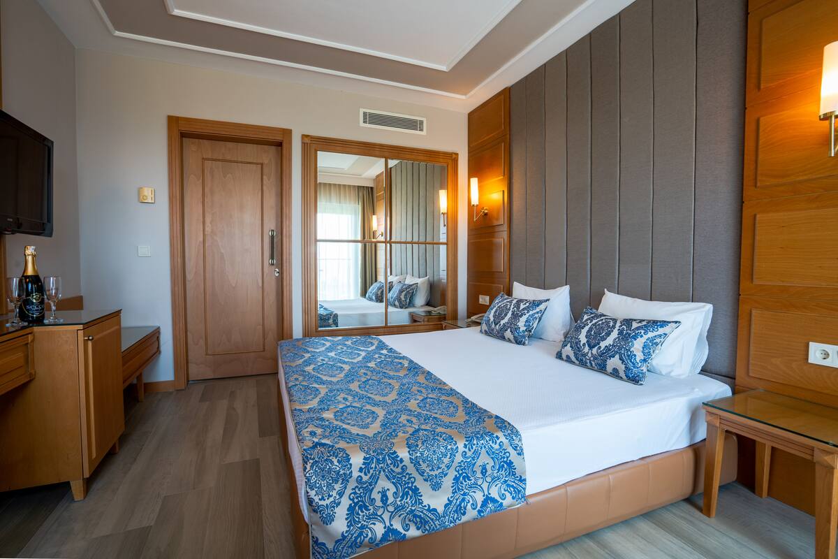 Habitación de hotel con una cama grande, muebles de madera, un espejo y una televisión.