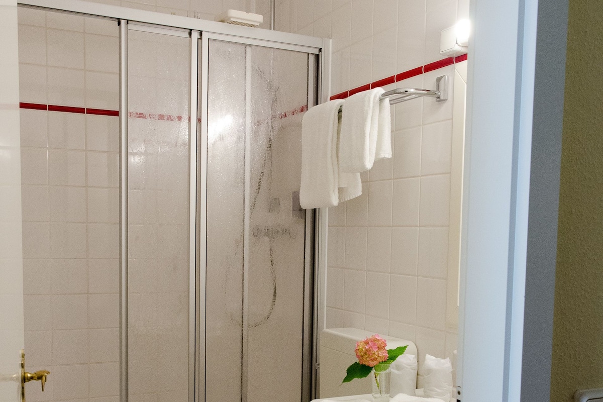 A bathroom with a glass-enclosed shower, a toilet, a sink with a vase of flowers, and a towel rack.