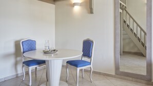 A dining area with a round table and two chairs, a light fixture on the wall, and a staircase in the background. - Skiathos Living by GHH (Skiathos)