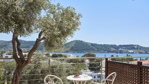 A balcony with a table and chairs, overlooking a scenic view of a lake and hills. - Skiathos Living by GHH (Skiathos)
