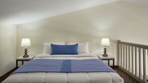 A bedroom with a bed, two bedside tables with lamps, a railing, and a sloped ceiling. - Skiathos Living by GHH (Skiathos)