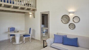 A dining area with a round table and chairs, a sofa with cushions, a balcony with a railing, and wall-mounted decorative plates. - Skiathos Living by GHH (Skiathos)