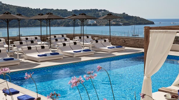 A poolside area with lounge chairs and umbrellas, a clear view of the sea, and a distant hill. - Skiathos Living by GHH (Skiathos)