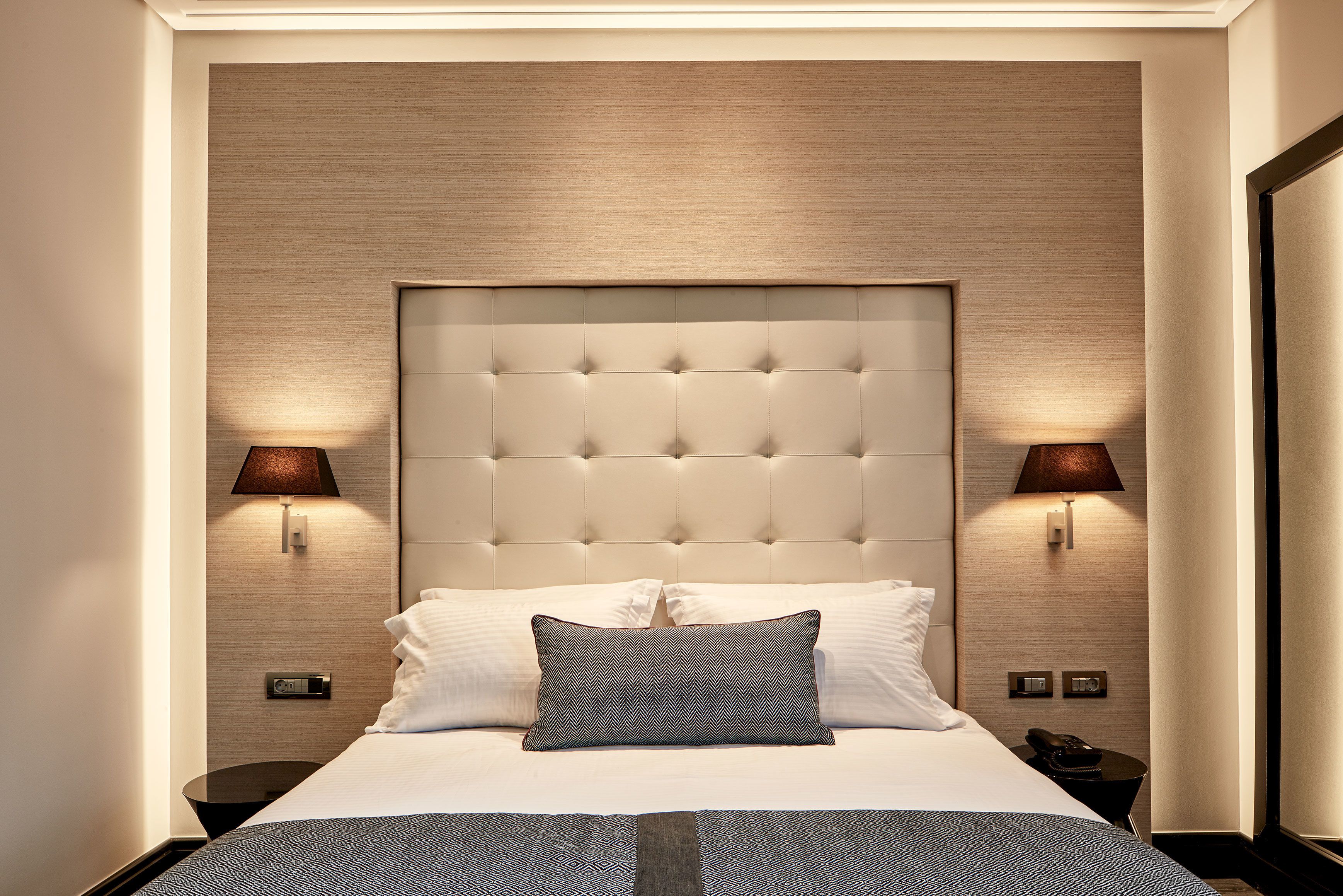 A neatly made bed with a tufted headboard, two bedside lamps, and a small table with a telephone.