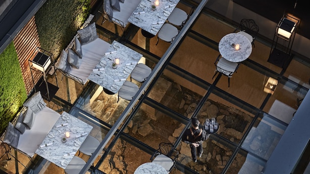 Un área de comedor al aire libre con varias mesas y sillas, piso de piedra y techo de vidrio.